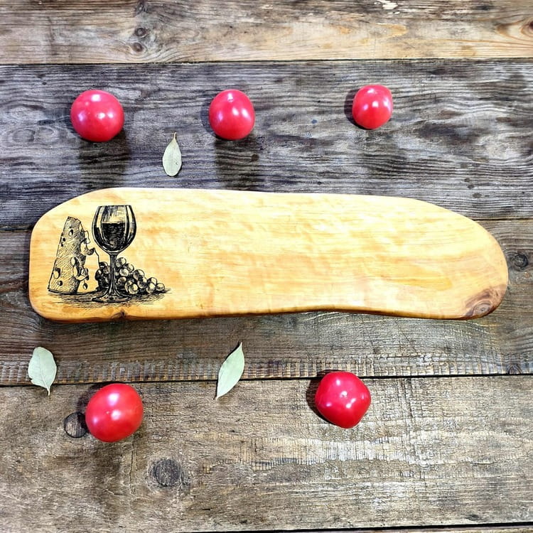 Deska drewniana do podawania serów z drewna jabłoni, po lewej stronie deska ma wypalony wzór, kieliszek wina, ser i winogrona. Wymiary deski 15x54cm