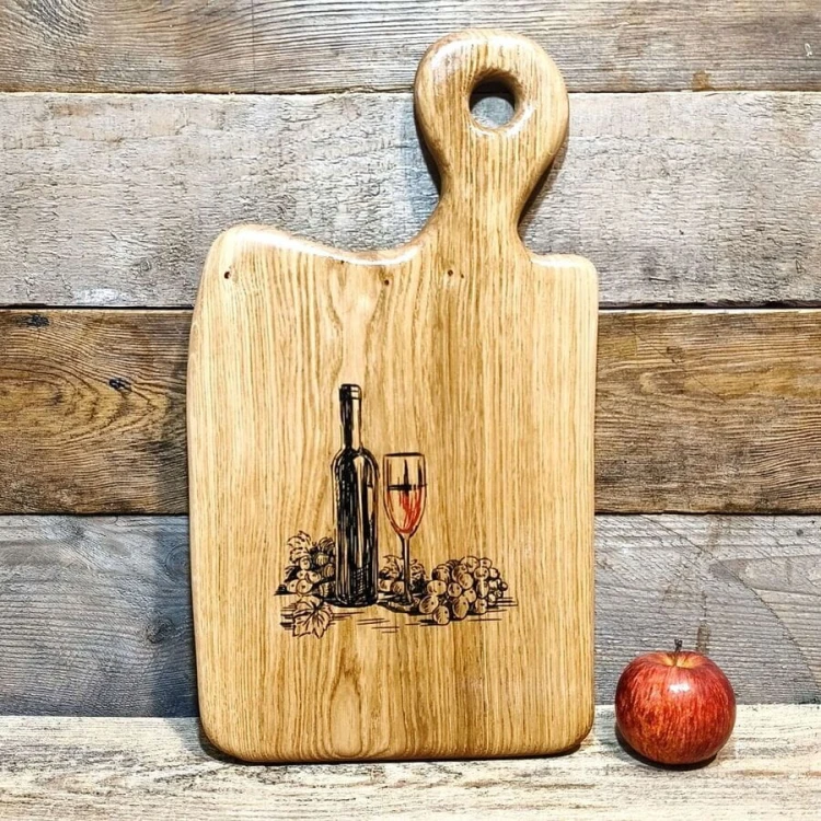 Ręcznie robiona drewniana deska  do serwowania z dębu. Deska jest  nieregularnym kształcie, deska posiada rączkę  i ozdobny grawer z butelką wina, kieliszkiem i winogronami  rozmiar deski 47x26cm