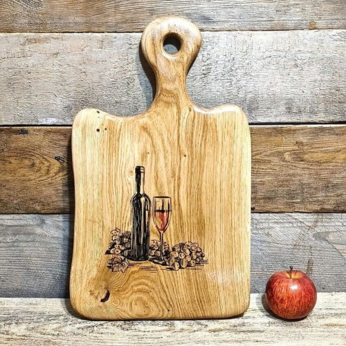 Ręcznie robiona drewniana deska  do serwowania z dębu. Deska jest  nieregularnym kształcie, deska posiada rączkę  i ozdobny grawer z butelką wina, kieliszkiem i winogronami  rozmiar deski 45x28cm