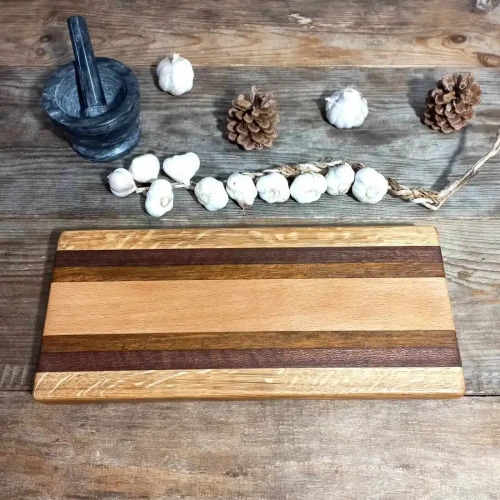 Długa deska do serwowania przekąsek wykonana ręcznie z kolorowych gatunków drewna: dębu, purpurowego amarantu, iroko i buku, z widoczną naturalną teksturą i połyskiem oleju. Wymiary deski 14x36cm