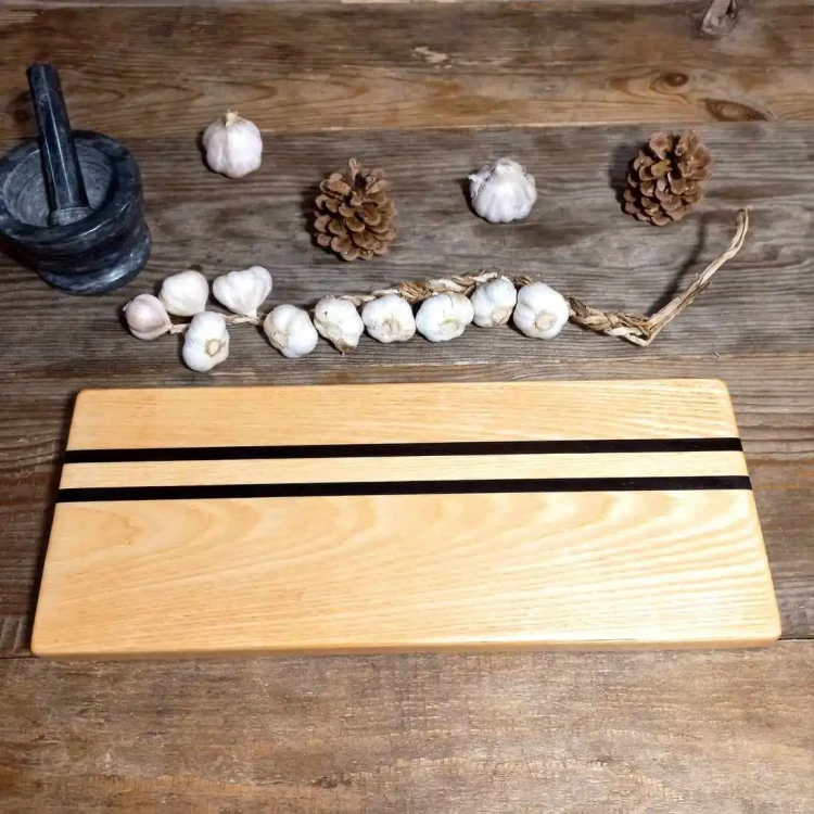 Ręcznie robiona deska do krojenia i serwowania przekąsek z jasnego jesionu i czarnego drewna wenge o wymiarach 16x40 cm, zaimpregnowana naturalnym olejem lnianym.